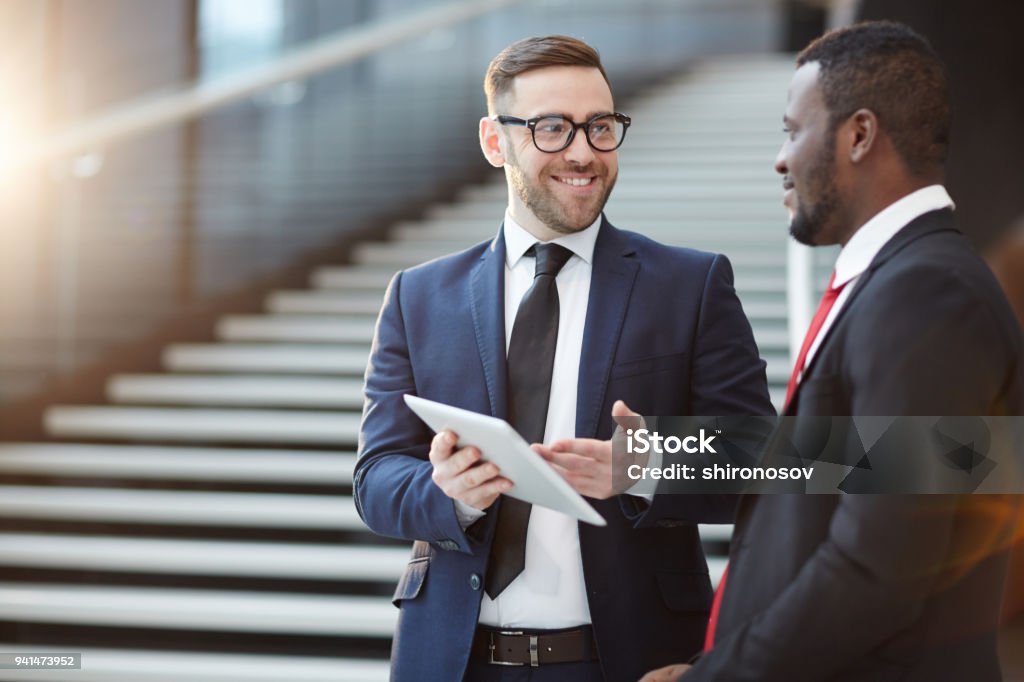 Showing information Successful delegate in elegant suit showing online data to his colleague or business partner at meeting in airport Business Person Stock Photo