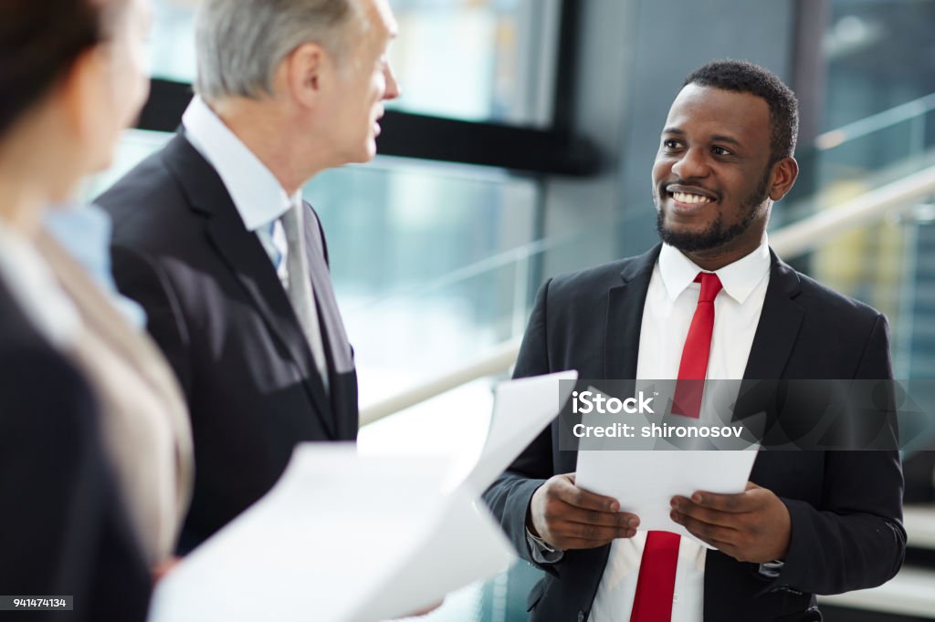 Listening to leader African-american businessman with paper listening to senior partner while discussing terms of contract at meeting Politician Stock Photo