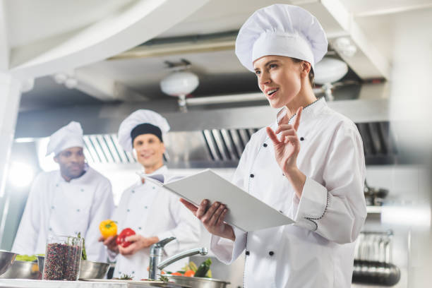 istock attractive chef holding recipe book and showing idea gesture at restaurant kitchen 941477628