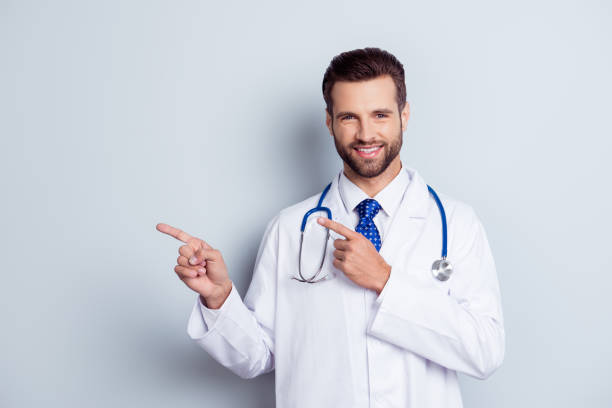 istock Glad dentist with beaming smile standing against white background and pointing on copy-space 941481114