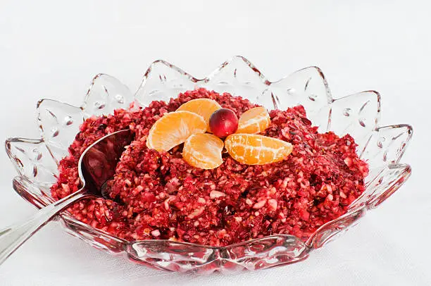 Cranberry relish made with fresh cranberries, oranges, and ginger in a pretty bowl on a white tablecloth.