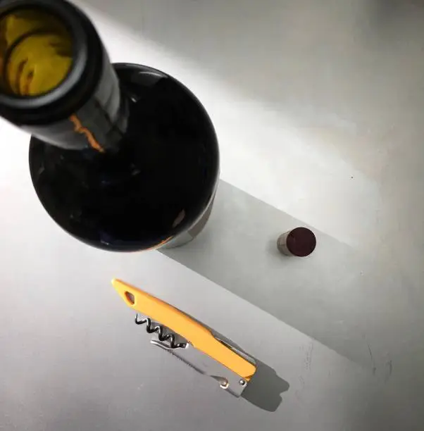 An open bottle of wine, it’s cork, and a corkscrew shown from above.
