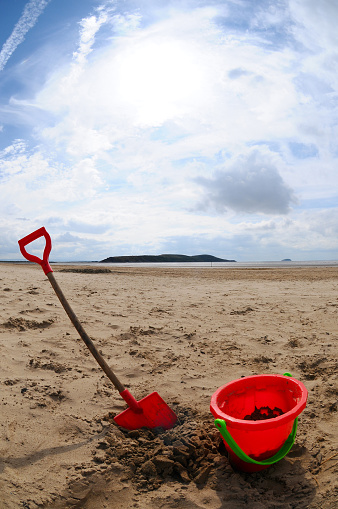 A childs plastic bucket and spade in the sand on a beach