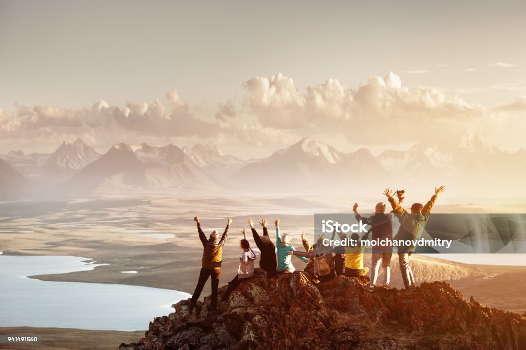 Big group of people success mountain top Big group of people having fun in success pose with raised arms on mountain top against sunset lakes and mountains. Travel, adventure or expedition concept Teamwork Stock Photo