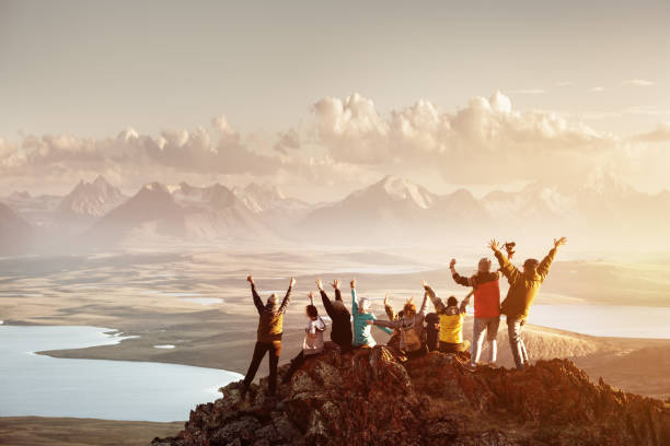 Big group of people success mountain top Big group of people having fun in success pose with raised arms on mountain top against sunset lakes and mountains. Travel, adventure or expedition concept mountain peak stock pictures, royalty-free photos & images