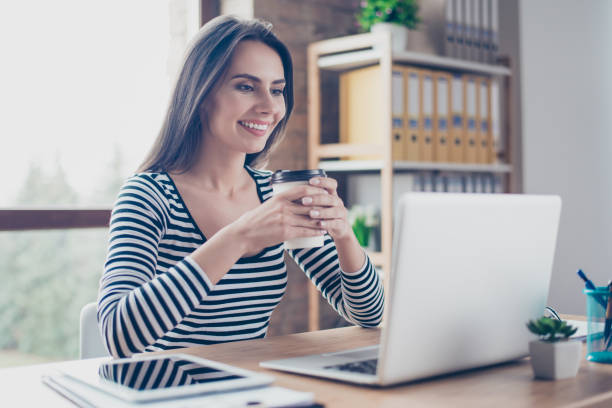 istock Pretty woman with beaming smile drinking coffee and reading news from the internet while having a break at work 941492084