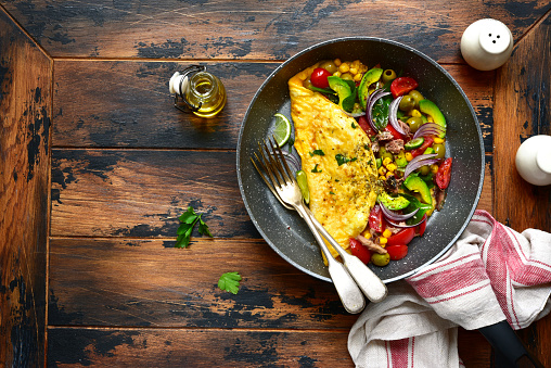 Omelette stuffed with vegetables in a black skillet for a breakfast over dark wooden background.Top view with copy space.