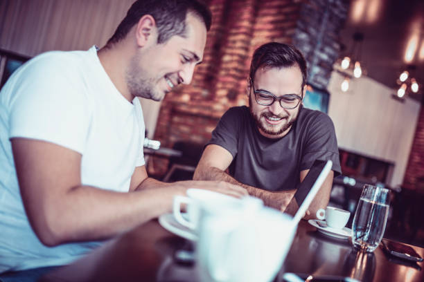 istock Two Smiling  Male Freelancers Drinking Coffee and Working In Coffee Restaurant 941496790