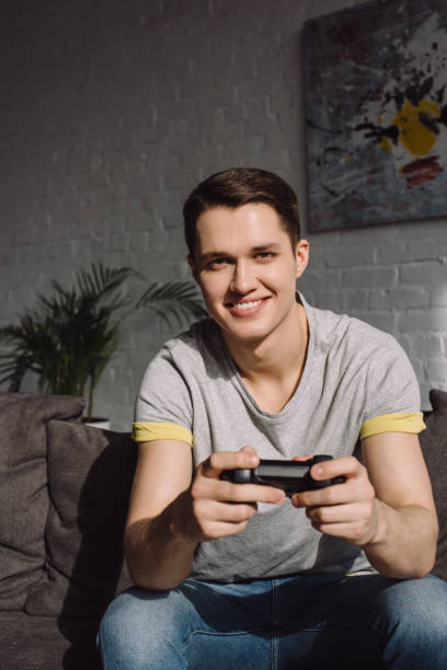 istock handsome man playing video game at home and looking at camera 941515524
