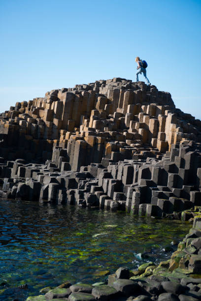 Giant's Causeway in Northern Ireland An American woman visiting Northern Ireland climbs to the top of a rock outcropping at Giant's Causeway in Northern Ireland. giants causeway photos stock pictures, royalty-free photos & images