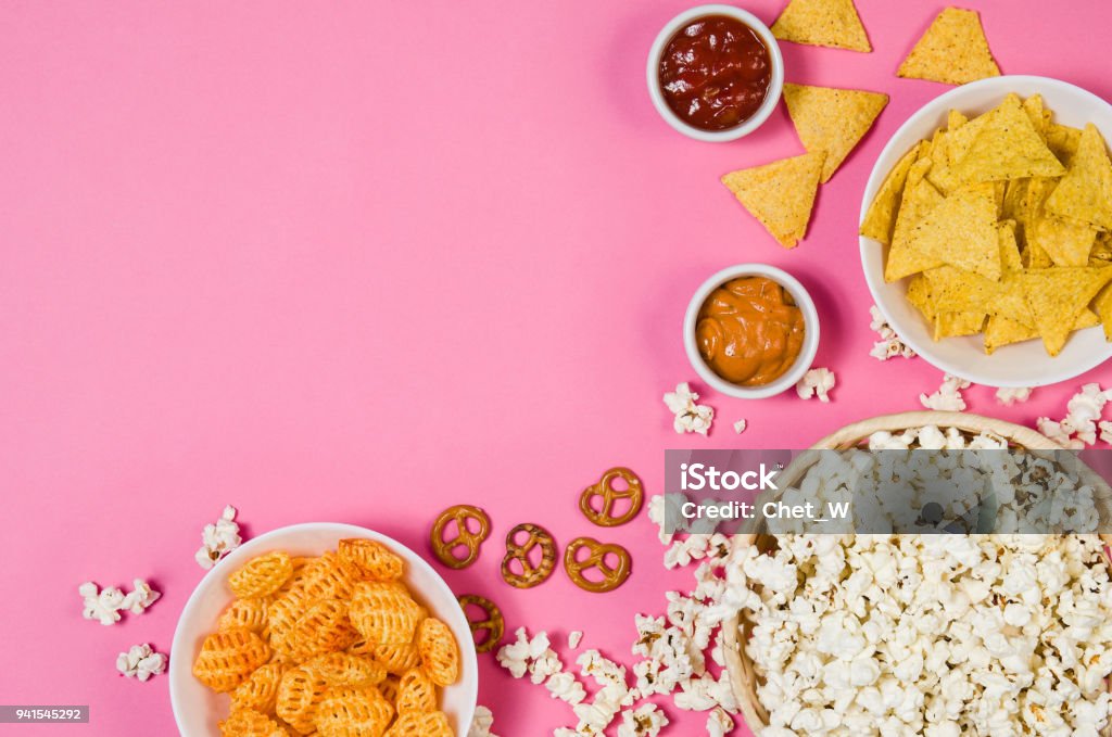 Popcorn and chips in bowl on pink background top view Fresh popcorn, snacks and chips in a bowl isolated on pink background top view. Frame composition with copy space. Movie watching concept Snack Stock Photo