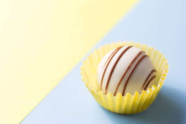 Homemade white chocolate truffle. Delicious sweet temptation. One candy ball on yellow and blue table.