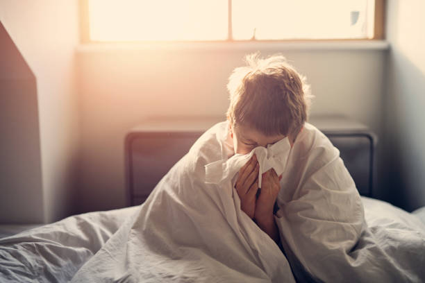 bambino malato sdraiato a letto e che soffia il naso - cold and flu flu virus sneezing illness foto e immagini stock