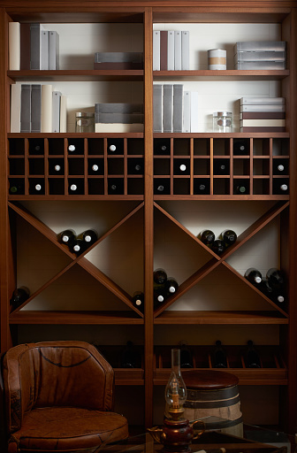 Bottles of white and red wine on a wooden shelf with books in private winery cabinet room interior