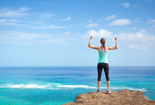 Young fit woman standing on the top of the mountain and overlooking the ocean.