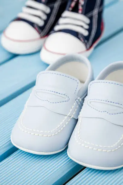 Pairs of dark blue,white baby sneakers and blue baby shoes over blue background