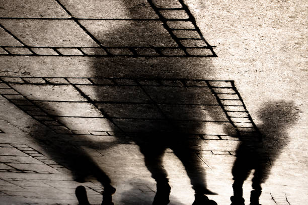 Silhouette shadow of a father holding hands with two small boys sons on city sidewalk in sepia black and white
