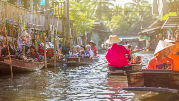 Damnoen saduak floating market, Thaïland Damnoen Saduak Floating Market, Thailand - November 29, 2015:   At the famous Damnoen Saduak Floating Market locals sell their fresh products (fruits and vegetables) aboard small wooden boats. It's a unique shopping experience.  Hats and colorfull umbrellas allow sellers to protect themselves from the country's warm sun. ratchaburi province stock pictures, royalty-free photos & images