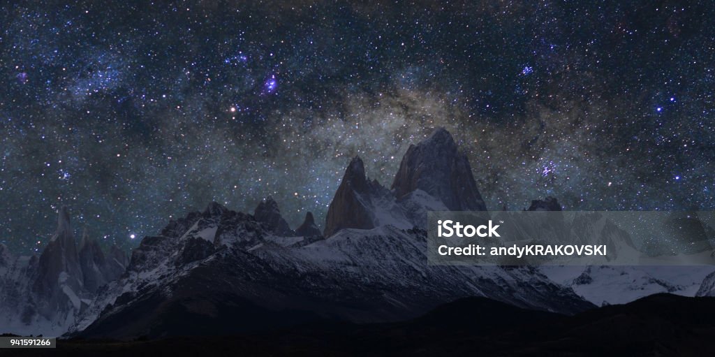 Andes at night, Patagonia Spectacular, granite towers of Cerro Torre, (to the left) and majestic Monte Fitz Roy (in a middle)  mountains in the Argentinian Patagonia visible at night under starry, moonless sky. This picture was taken on a cloudless night of March 22, 2018 just few days after the New Moon, when the brightest part of Milky Way near the Sagittarius and Scorpius constellations was shining right behind Mount Fitz Roy (3,405 m/11,171ft). The “star” on the horizon, in a valley to the right of Cerro Torre (3,128 m/10,262 ft) is actually the planet Saturn, and further up, kind of reddish, is the bright planet Mars. These mountains form part of the Los Glaciares National Park (Parque Nacional Los Glaciares), near the village of El Chalten, Argentina. Night Stock Photo