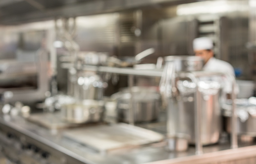 Defocused chef preparing food in commercial stainless steel kitchen in restaurant