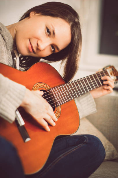 istock Young woman playing guitar at home 941594608