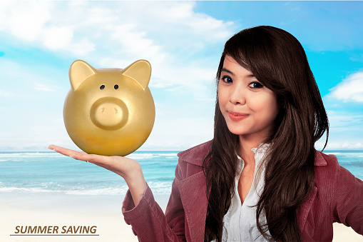 Smiling asian business woman holding piggy bank. Summer saving concept