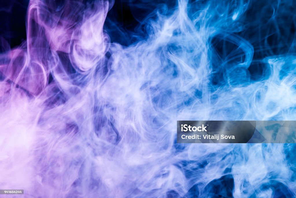 Background from the smoke of vape Dense multicolored smoke of   blue and purple colors on a black isolated background. Background of smoke vape Abstract Stock Photo