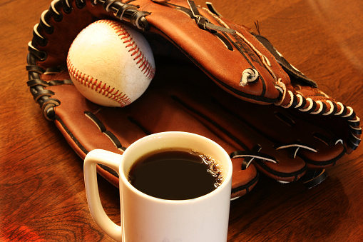 Baseball and leather ball glove with coffee cup on wooden table.