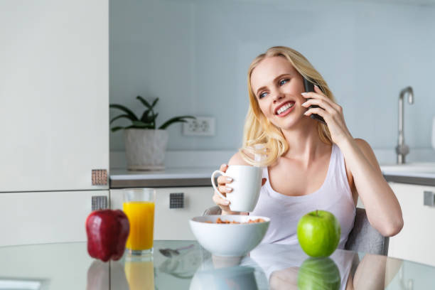 istock beautiful smiling young woman drinking coffee and talking by smartphone during breakfast 941683846