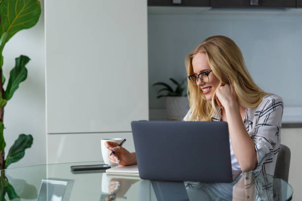 istock smiling young woman in eyeglasses using laptop and taking notes while working at home 941684186