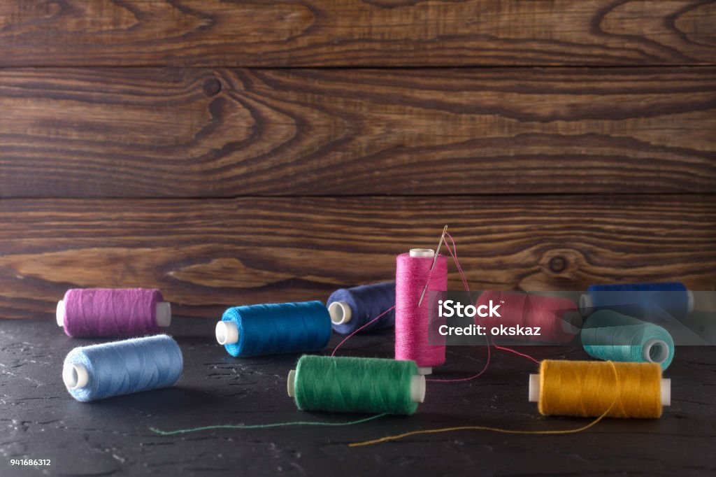 Sewing thread on coils, fabric, needles for sewing on wooden background. Set for tailoring products, knitting, hobbies and handmade, dressmaker, sewing accessories. Adhesive Tape Stock Photo