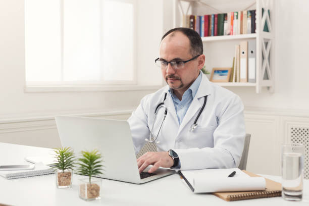 istock Serious doctor in glasses typing on laptop 941690964