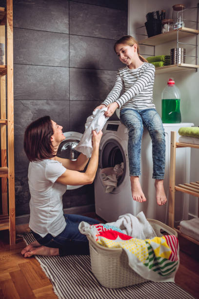istock Mother and daughter putting clothes in a washing machine 941691484