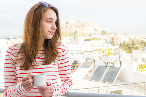 Young woman enjoying coffee on the balcony and the city view of Parthenon in Athens