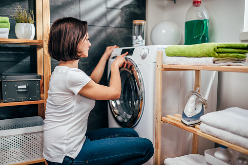 Woman wearing white shirt choosing program on washing machine in laundry room