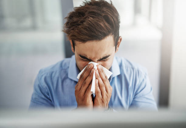 Influenza is one serious business Shot of a young businessman blowing his nose with a tissue at work cold virus stock pictures, royalty-free photos & images