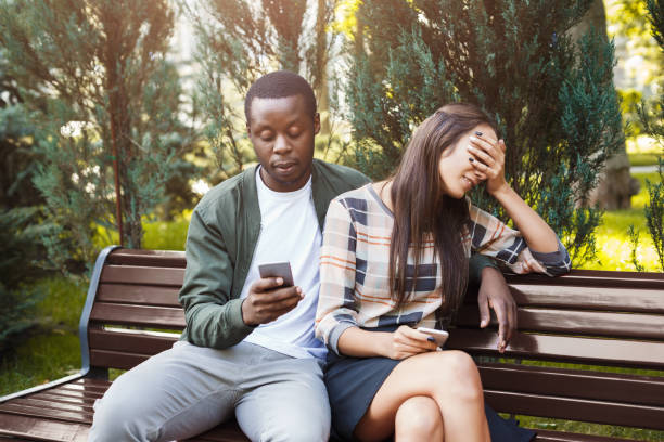 mujer sentada en el parque con hombre con smartphone - african descent addiction african ethnicity rudeness fotografías e imágenes de stock