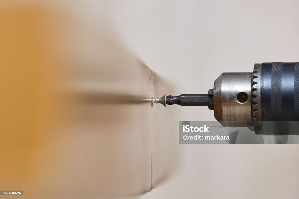 Worker screwing a screw into a wooden table with an electric screwdriver. Screw Stock Photo