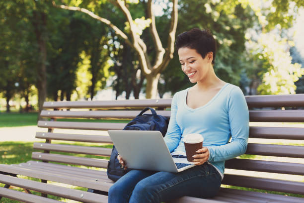 istock Attractive smiling female freelancer working on a laptop and drinking coffee outside 941723202