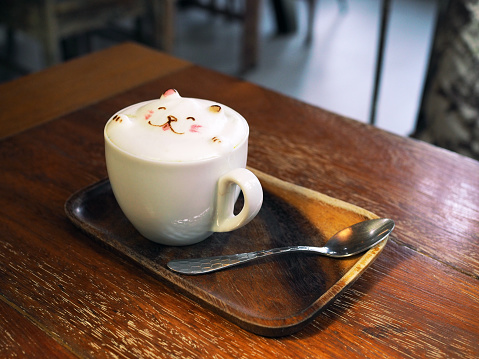 A mug of cute bear shape foam on tasty hot mocha on wooden tray with selective focus.