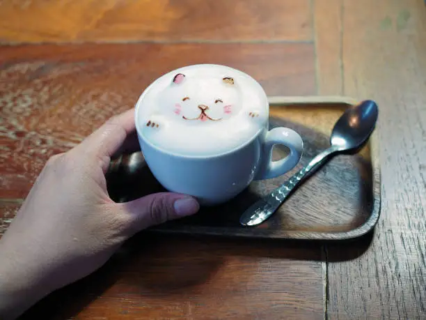 Photo of A mug of cute bear shape foam on tasty hot mocha on wooden tray.