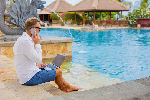 Businessman working at poolside while on vacation