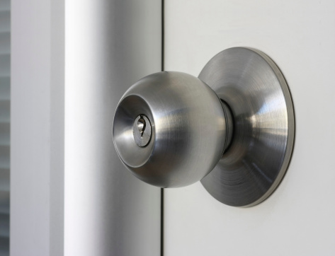 Close-up side view photo of a brown metal vintage door knob and skeleton keyhole on an old wooden white painted door with gray painted wood door trim and copy space