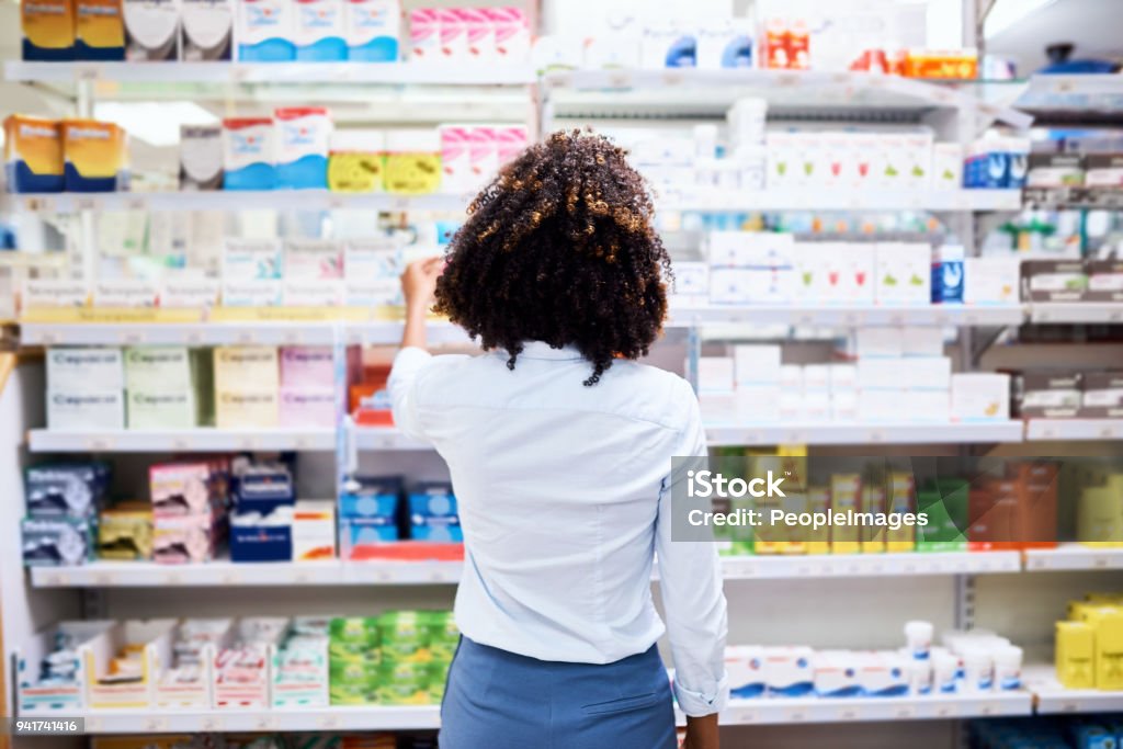 So many choices Rearview shot of a young woman looking at products in a pharmacy Pharmacy Stock Photo