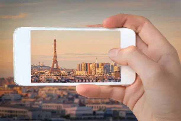 Photo of Closeup of a hand with smartphone taking a picture of  Paris with the Eiffel tower at sunset,  France