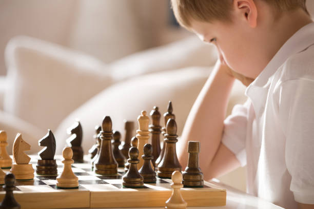 istock Boy playing chess in the room. Little clever boy concentrated and thinking while playing chess at home. 941749362