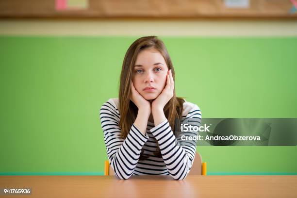 Sad Student Sitting In Classroom With Her Head In Hands Education High School Bullying Pressure Depression And Teenagers Concept Stock Photo - Download Image Now
