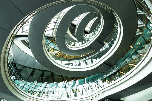 Wide angle color image depicting ultra modern contemporary interior architecture in City Hall (a public building in London that is open to the public) in London, UK. Looking up we can see a modern spiral staircase winding around the entire building, and also the windows that surround the building, letting in as much natural light as possible. Lots of room for copy space.