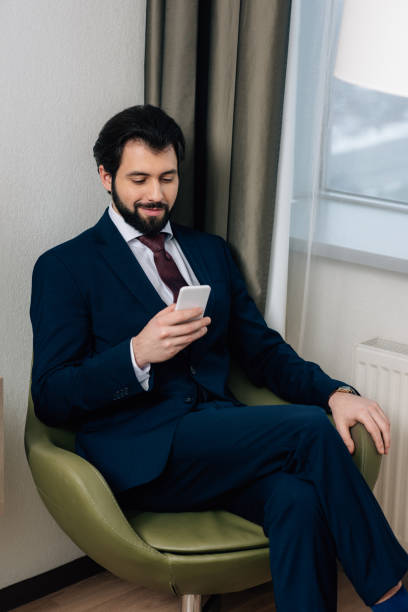 istock handsome businessman using smartphone while sitting in armchair 941775014