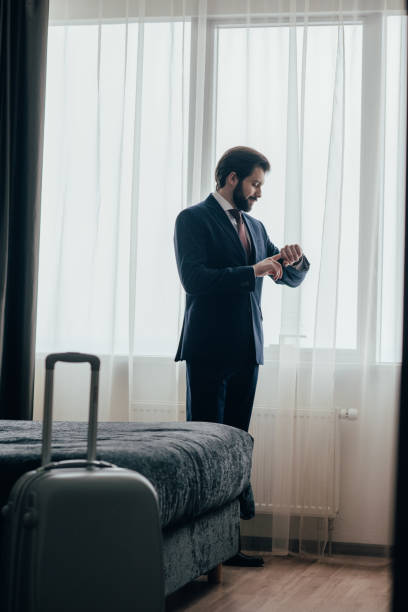 istock handsome businessman in hotel suite looking at watch while standing near window 941778884